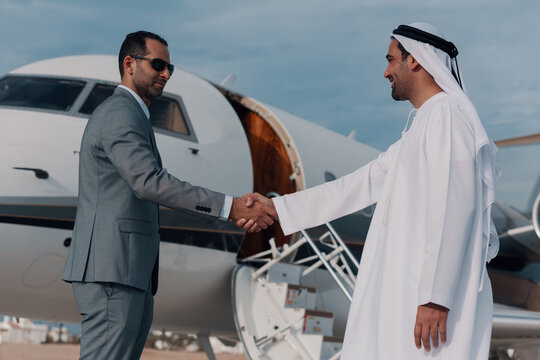 Business handshake between businessman and Emirati partner at private jet boarding for luxury travel deal