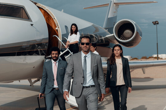 Business executives and corporate team walking confidently from private jet on airport tarmac during luxury travel
