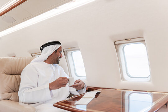 Businessman in traditional white robe enjoying coffee while traveling on a luxury private jet