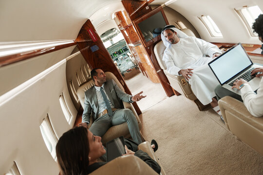 Business meeting in a private jet cabin with executives and a man in traditional white robe