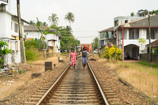 Sri Lanka - 11 February 2026: View of two people walking along a railway track passing through a residential neighborhood with houses and palm trees.