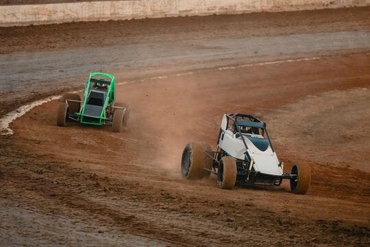 Sprint cars race on a dirt track, kicking up dust as they speed around a corner