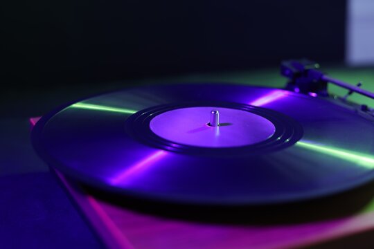 Modern turntable with vinyl record on table in color lights, closeup