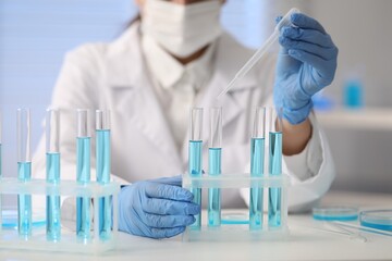 Fototapeta premium Scientist dripping blue liquid into test tube at white table in laboratory, closeup