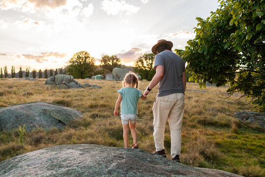 little girl on an outdoor adventure with her dad over lichen covered boulders in park