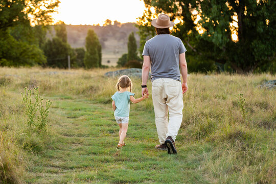 Dad on walk with young daughter walking away down grassy path in recreational area