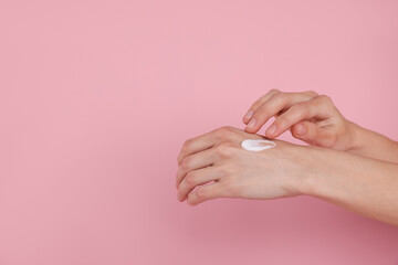 Fototapeta premium Woman applying hand cream on pink background, closeup. Space for text