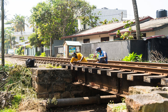 Sri Lanka - 31 January 2026: View of two railway workers performing maintenance on a track bridge near residential houses and palm trees.
