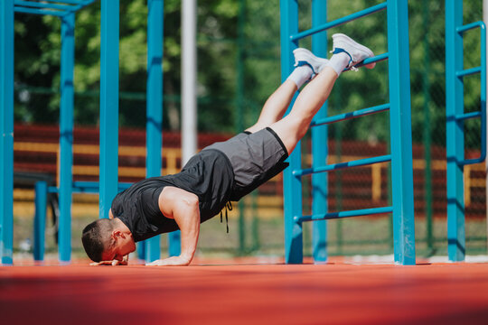 Man performs elevated push-up with feet on bars in an outdoor calisthenics park. Outdoor athlete trains core and upper-body strength using bodyweight on parallel bars.