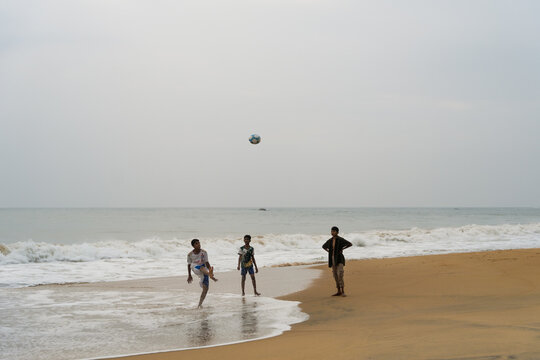 Sri Lanka - 30 January 2026: View of three boys playing football on a sandy beach with ocean waves and an overcast sky.