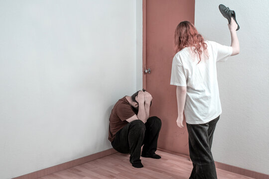 Female aggressor raising a shoe over a frightened man, relationship violence, coercive control and intimidation indoors.