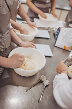 Hands are mixing dough for sourdough bread and pizza in a busy bakery kitchen during a baking class