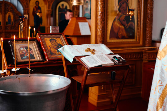 Orthodox church interior with candles, icons, open prayer book, wooden stand and baptism font in warm sacred light.