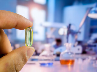 The image shows a hand holding a capsule against the background of a blurred laboratory room. © Valeryi