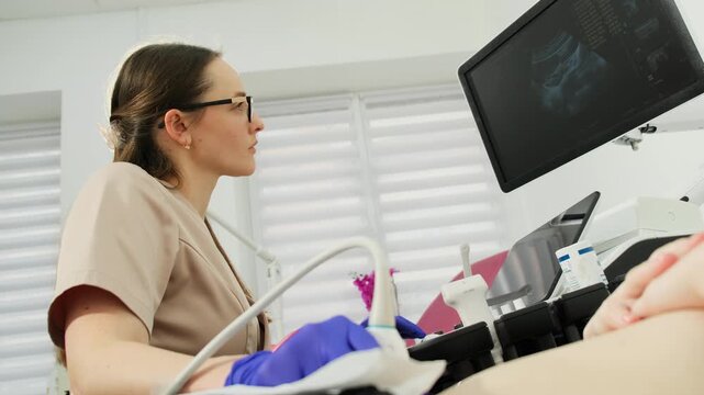 Gynecologist reviews monitor during pelvic ultrasound scan. Specialist guides sensor steadily studying diagnostic image closely in clinic