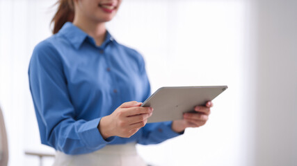 young Asian businesswoman professional using digital tablet computer reading business report standing office workplace bright modern corporate environment © Pichsakul