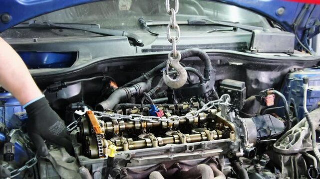 Mechanic holds chain to further extract engine from compartment. Removing part from car allows for inspection to identify extent of damage