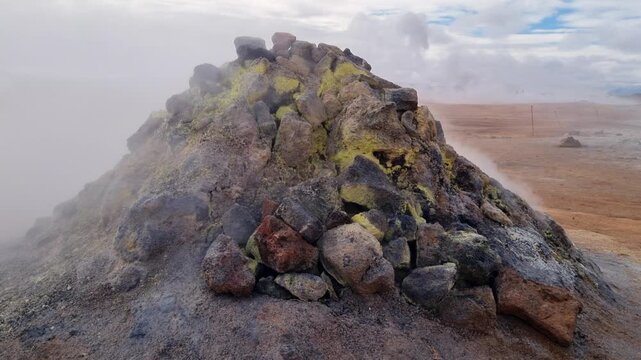 Volcanic landscape with sulfur deposits on rocks at a geothermal area. Steam and smoke rising from a fumarole in the Icelandic highlands