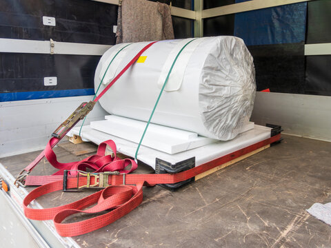 Large wrapped industrial cargo roll strapped with red ratchet belts inside a transport truck. The image represents freight shipping, cargo safety, logistics, delivery service, warehouse transport, and