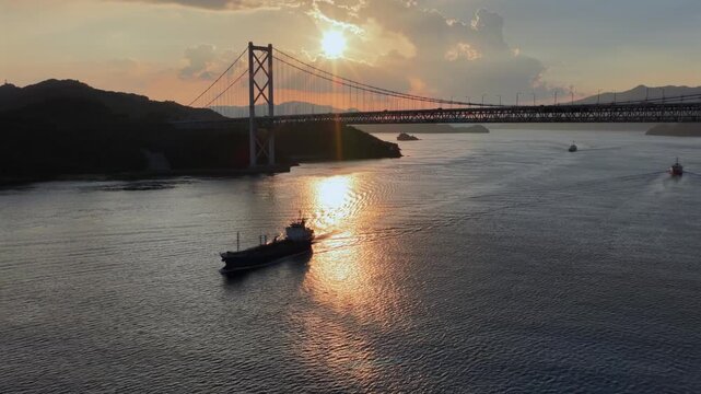 Boat passing beneath Innoshima Bridge at sunset with dramatic backlight in Japan