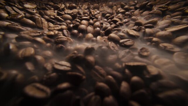 Wide angle sliding shot of roast coffee beans with gentle smoke on a dark background. Fresh coffee beans roasting with aromatic steam slow motion video 120 fps. 