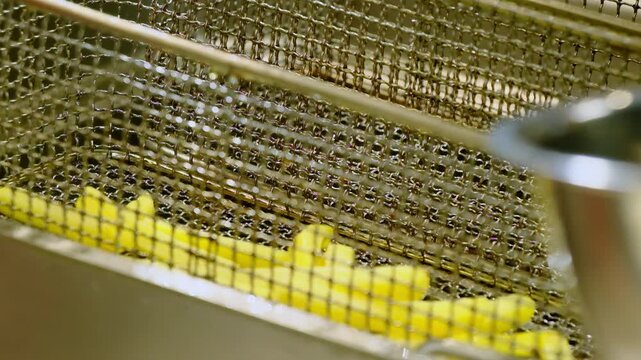 Raw potato sticks fall down into steel strainer over bathe with hot oil closeup. Cooking French fries for cafe guests in fast food restaurant