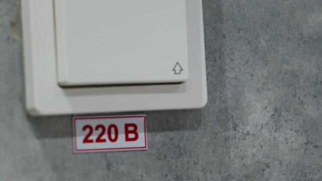 Button for switching light on and off placed neatly on wall. Voltage label shows electrical voltage. Modern switch for lighting system