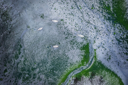 Aerial view of small white boats moored on the textured tidal flats of Bull Island with vibrant green algae and grey sand patterns in County Dublin, Ireland.