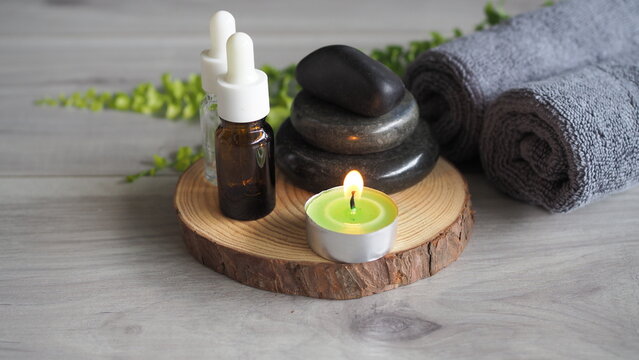 Spa wellness composition with essential oil bottles, hot stones, rolled towels and candle on wooden tray. Relaxation therapy, aromatherapy and luxury self care lifestyle concept.