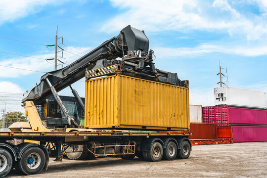 Reach stacker loading yellow shipping container onto truck at industrial terminal port