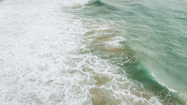 Aerial view of turquoise ocean waves crashing with white foam and surf, Sagres, Faro, Portugal.