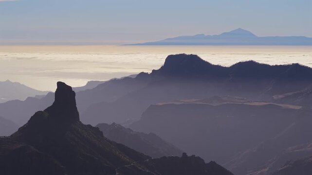 Stunning aerial perspective of Gran Canaria's mountain landscape, featuring Roque Bentayga and Mount Teide above a sea of clouds at dawn