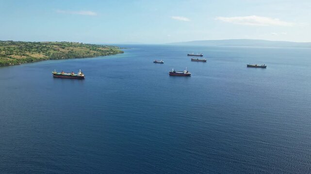 Aerial drone footage of cargo vessels at anchor, nearby the dock harbor in Calabai port, Sumbawa island, Indonesia, blue water, and coast, Mojo island national park in the background