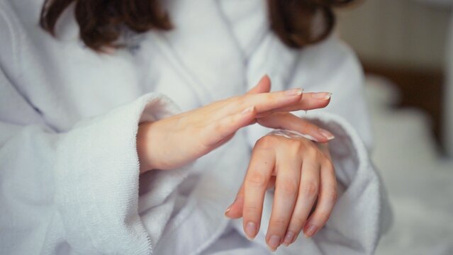 Woman in a soft bathrobe massaging nourishing cream into delicate hands during a morning skincare ritual for hydrated, smooth skin and gentle self care at home