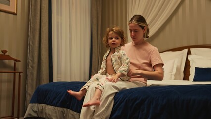 Obraz premium Mother preparing toddler daughter for a relaxing night, sitting together on a comfortable bed in matching pajamas while creating cherished family moments