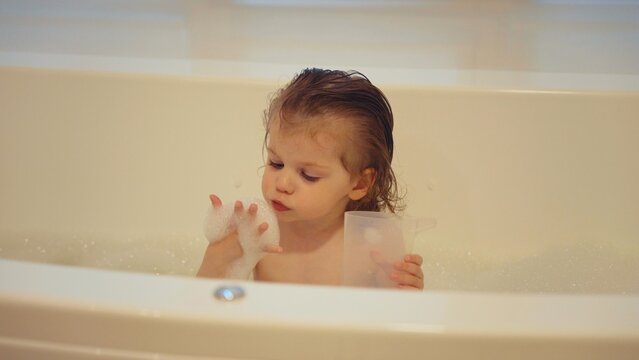 Toddler splashing joyfully in a bubbly bathtub, playing with soap and water during bath time, carefree childhood moment of hygiene, fun, and family bonding