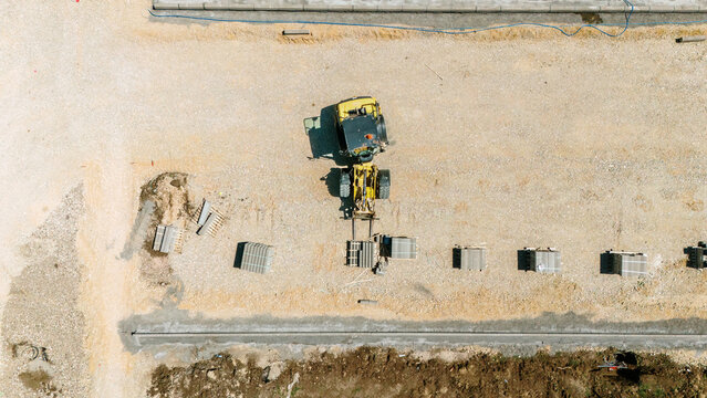 Aerial view of a yellow wheel loader moving materials on a construction site with stacks of paving stones Pancevo, Vojvodina, Serbia.