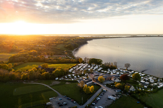 Aerial view of Bockholmwik campsite and the Flensburg Fjord at sunset with parked caravans and lush green fields in Munkbrarup, Schleswig-Holstein, Germany.