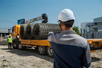 Construction site manager pointing and directing worker for unloading steel wire mesh delivery from truck. Industrial infrastructure project, logistics and supply chain management. © VStudio