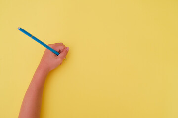 Left-handed child's handwriting with a blue pencil on a yellow background. Left-handed person's day