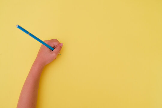 Left-handed child's handwriting with a blue pencil on a yellow background. Left-handed person's day