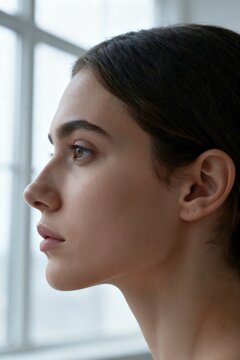 Thoughtful young French woman in her early twenties looking away in serious profile portrait with natural window lighting.