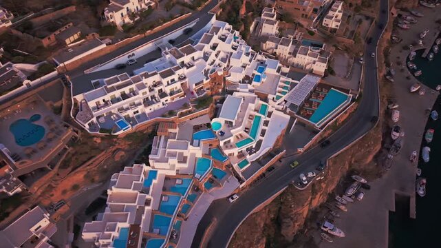 Birds-eye view drone footage of luxury hotel resort architecture with swimming pools at sunset. Geometric pattern of white villas and swimming pools during golden hour in Mykonos, Greece.