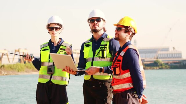 Team male and female engineers in uniform safety equipment stand surveying the area infrastructure development projects including the construction deep sea distribution port land bridge and shipyard.
