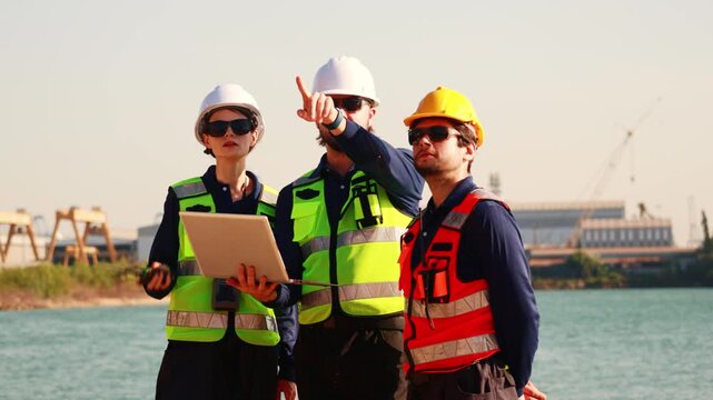 Team male and female engineers in uniform safety equipment stand surveying the area infrastructure development projects including the construction deep sea distribution port land bridge and shipyard.
