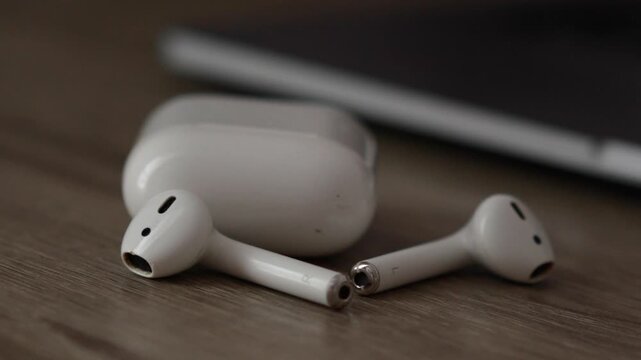 Modern wireless earbuds scattered on a table next to a white plastic case for storing them