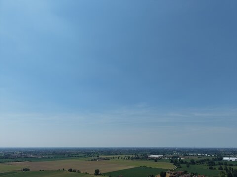Vast Horizon of Summer Sky: An expansive aerial view captures rolling green fields and distant rural landscape under a clear, bright blue summer sky, stretching towards the horizon.