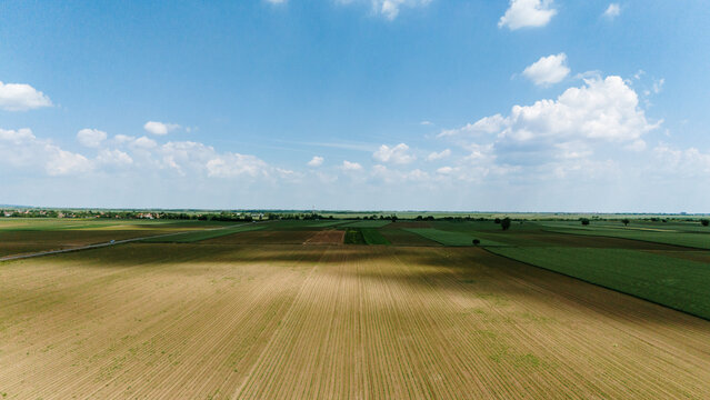 Aerial view of vast agricultural fields and patchwork farmland under a blue sky with scattered clouds in Novi Sad, Vojvodina, Serbia.