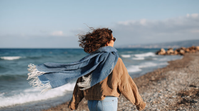 Woman beach seashore walking wind scarf coastal Young woman walking along seashore with windblown scarf, calm mood