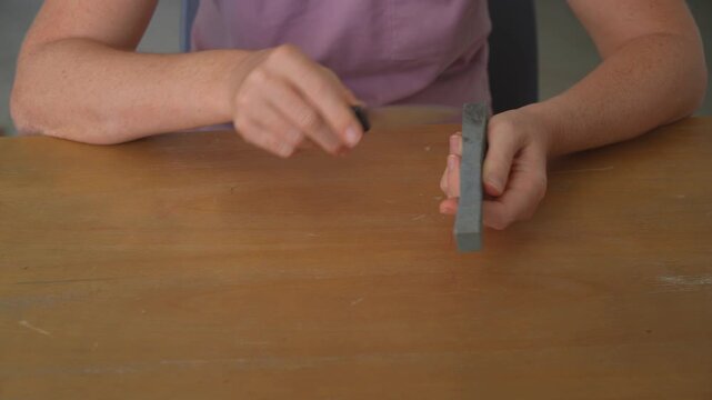 Close up woman sharpening knife with clear sound. Hands honing blade on sharpener at kitchen table. Cooking preparation, tool maintenance, safety and everyday routine concept